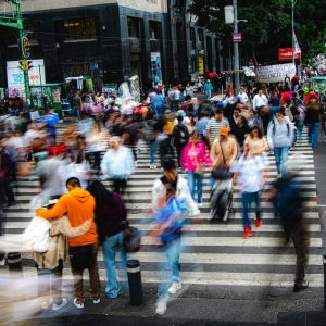 A bustling city street with a crowd of pedestrians crossing a zebra crossing, showcasing urban life.