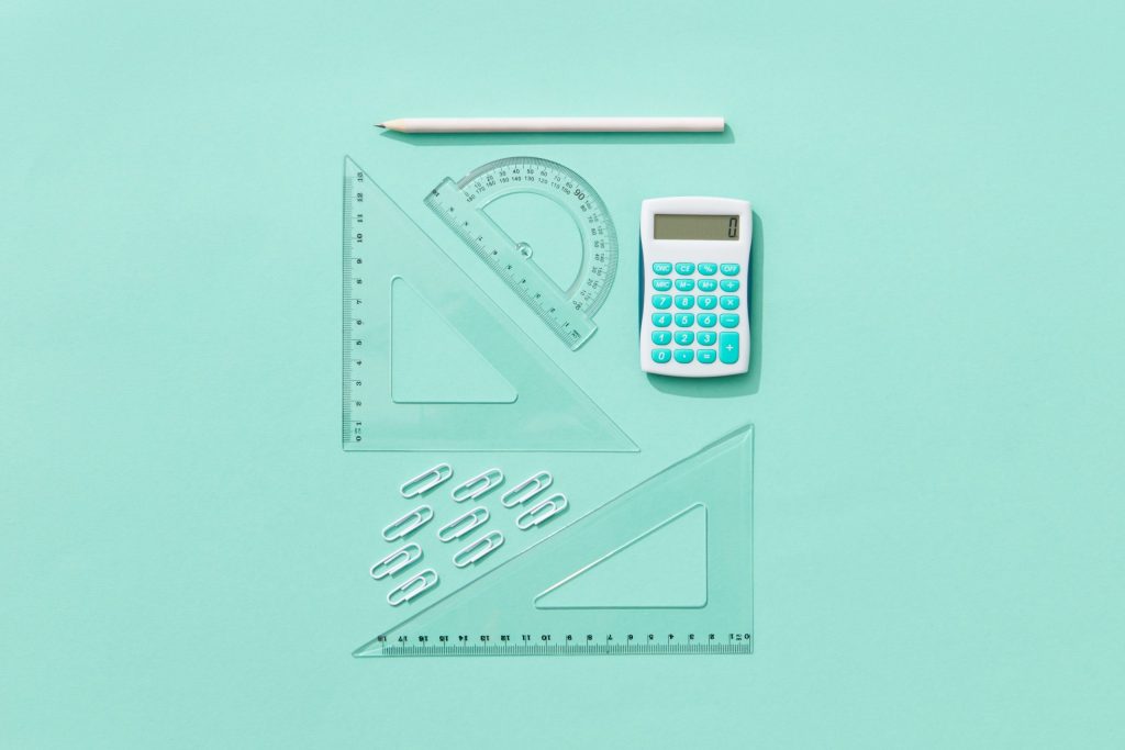 Flat lay of school supplies including calculator, rulers, and pencil on pastel background.